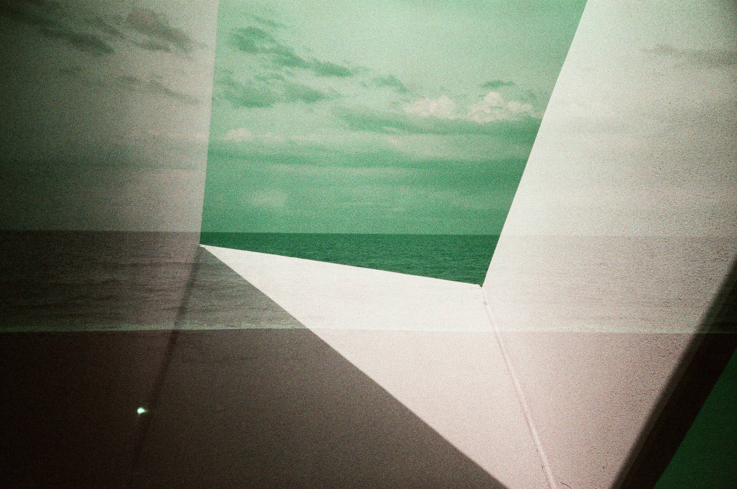 Two overlaid images of a building an the horizon at the beach looking out over the water with weird shifted purplish colors